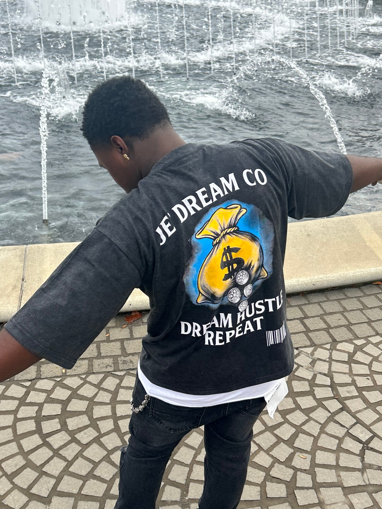Person wearing a black acid wash t-shirt with a colorful graphic design on a stone pavement.