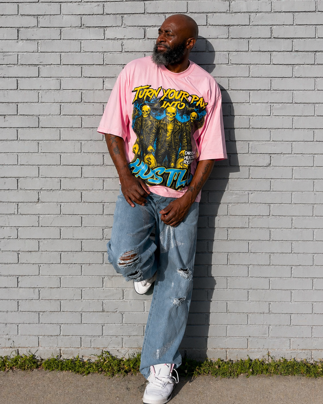 Model wearing a pink turn your pain into hustle boxy t-shirt with graphic design and text, standing against a gray brick wall.