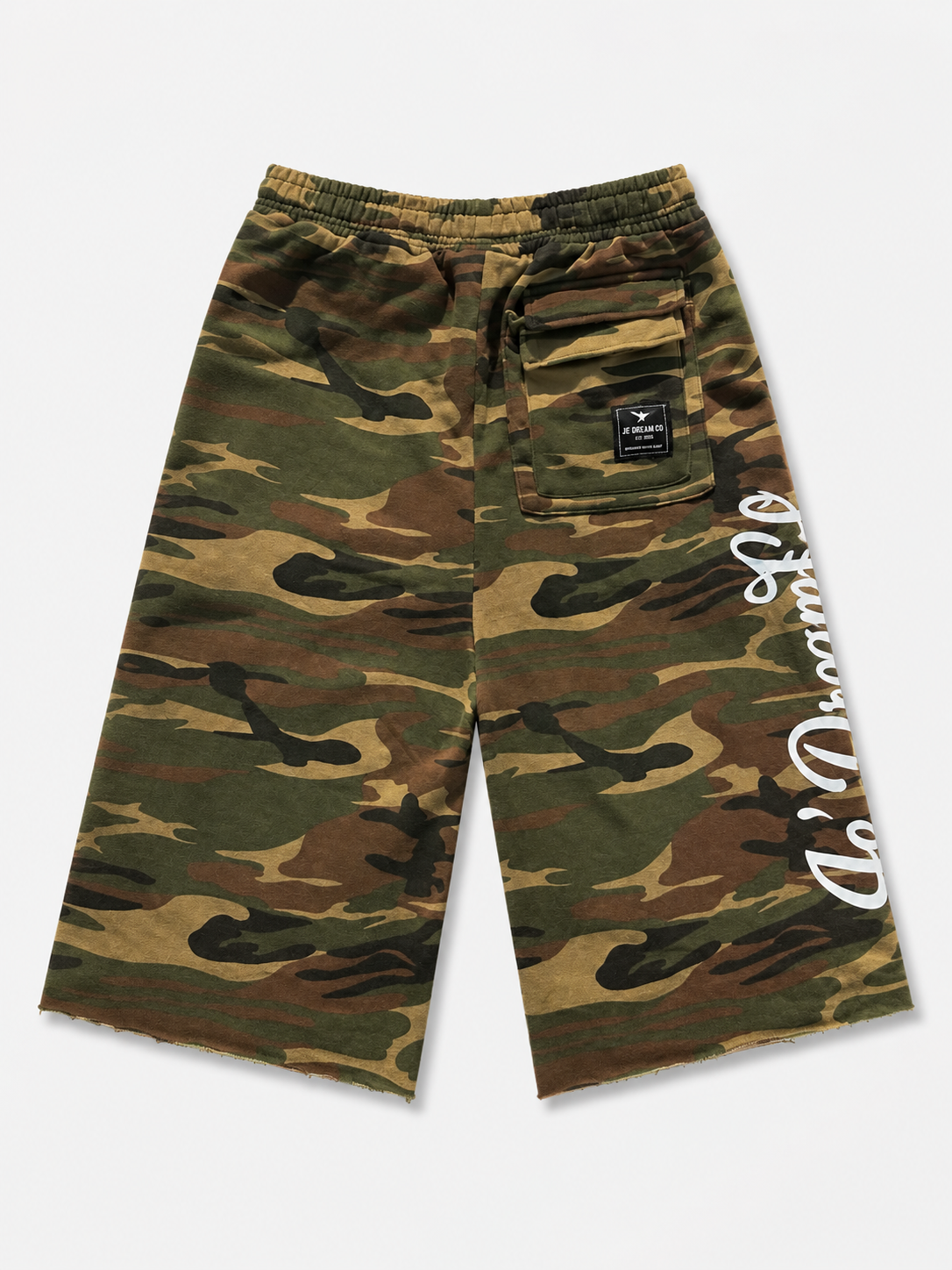 A pair of camouflage shorts in green, brown, and tan, featuring a white script logo printed vertically on the left leg and a black brand patch on the back pocket.