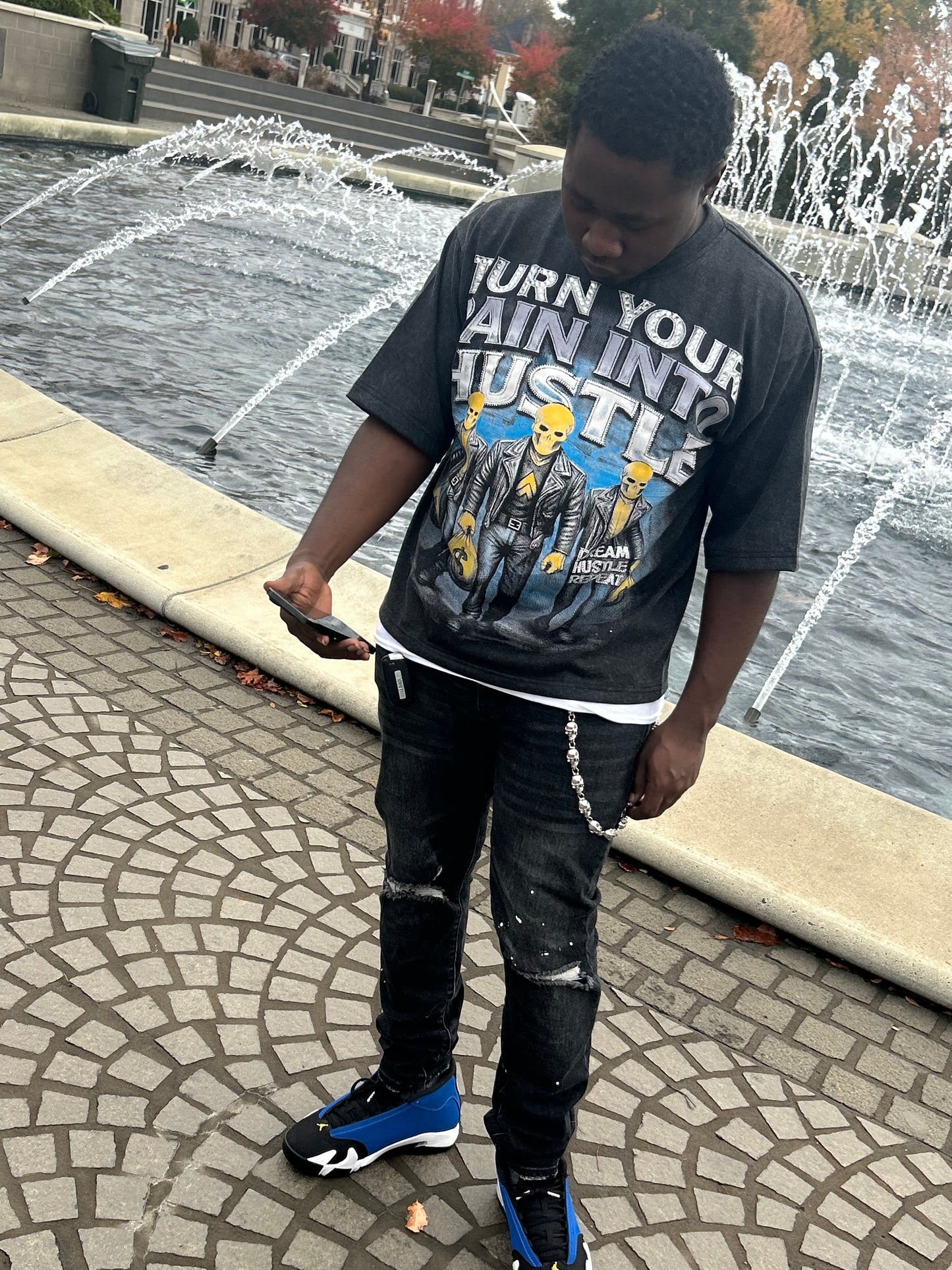Model wearing black acid wash turn your into hustle graphic t-shirt and jeans standing by a waterfront.