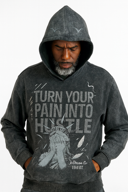 Man wearing a black acid wash hoodie with 'Turn Your Pain Into Hustle' text and graphic design.