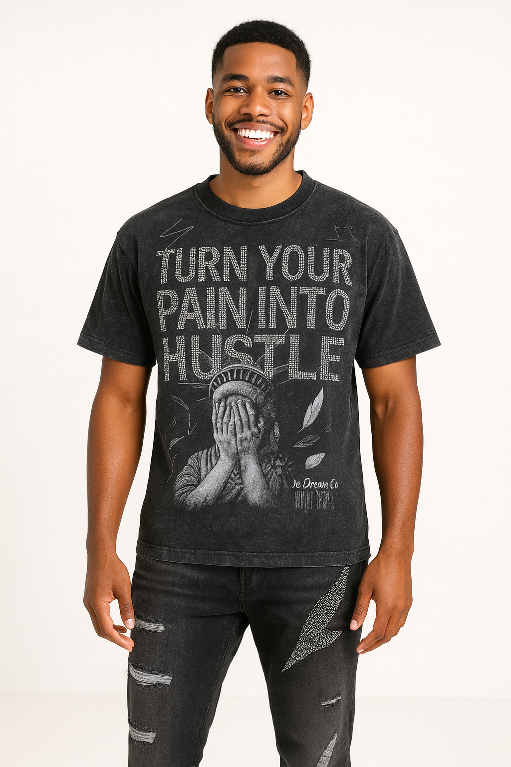 Man wearing a black acid wash t-shirt with turn your pain into rhinestones text and graphic design on a plain background