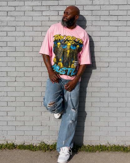Model wearing a pink turn your pain into hustle boxy t-shirt with graphic design and text, standing against a gray brick wall.